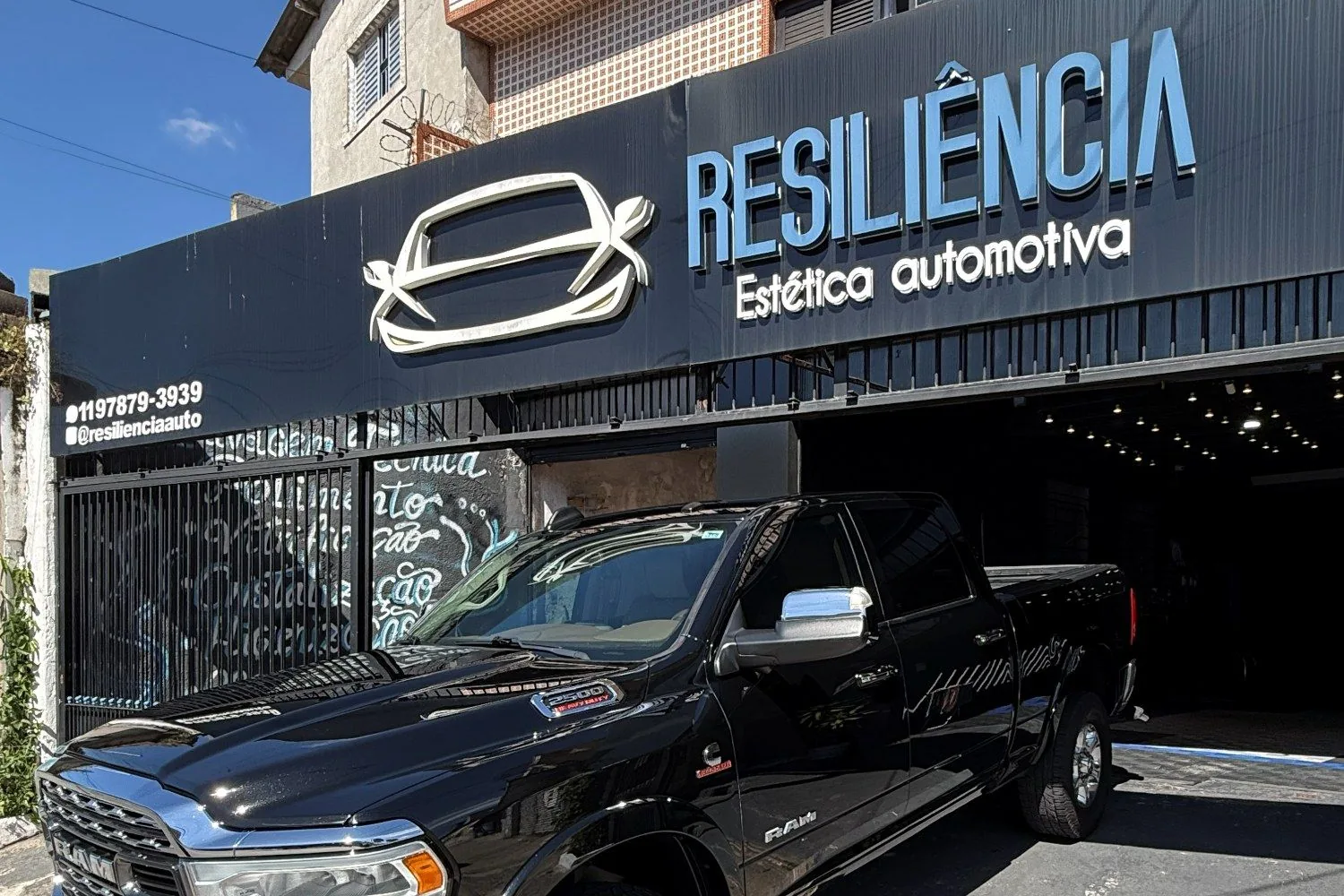 Fachada da Resiliência Estética Automotiva, com o letreiro da loja e uma picape preta estacionada na entrada do box.